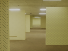 An image of the Backrooms. A large, open room with carpet, fluorescent lights and yellow wallpaper. A gap in the wall shows similar rooms extending without limits.