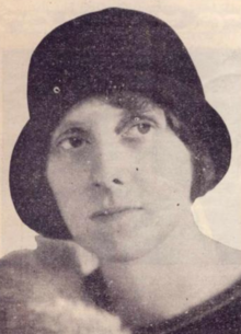 A white woman wearing a dark cloche-style hat, with the front of the brim folded upward