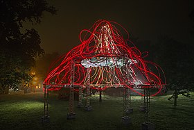 Glowing red tubes form an open dome in a park at night.