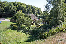 Et gammelt hus omgivet af vegetation midt i en lille dal.
