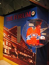 Foto de uma seção da parede dedicada ao Fórum de Montreal: foto colorida do fórum, montada com o título O Fórum e um disco com o logotipo do Montreal Canadiens;  em um canto, uma camisa com o número 14 do Montreal Canadiens.