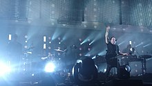 Un homme habillé de noir lève le poing sur le devant d'une scène de concert