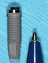 A standard 13 mm root form dental implant with pen beside it for size comparison