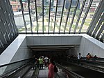 Eskalator menghala bawah ke aras legar stesen MRT daripada jejambat pejalan kaki.