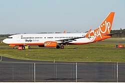 A large white plane facing left on a runway, with the bottom and tail painted in orange