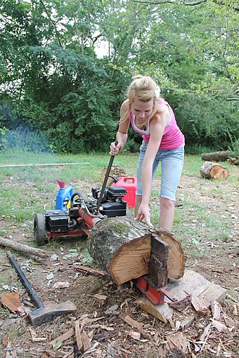 A woman using a gas powered log splitter to split firewood.