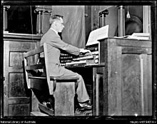 A black and white photo of a man playing the organ showing the keyboard and the pedals