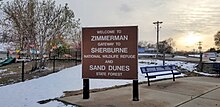 cartello con la scritta "Benvenuti a Zimmerman, porta d'ingresso allo Sherburne National Wildlife Refuge e alla foresta statale delle dune di sabbia"