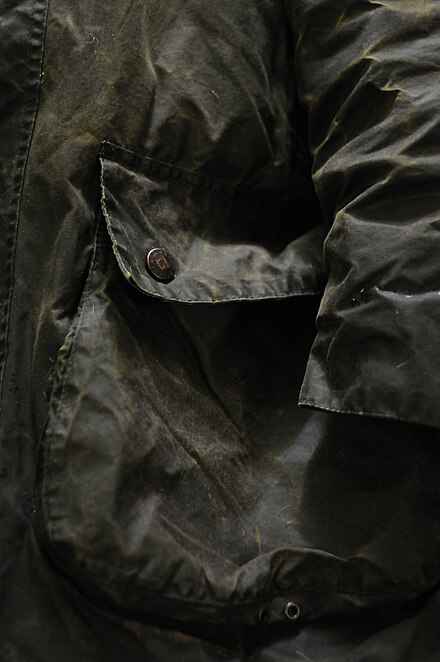 The pocket of a green Barbour jacket showing wear.