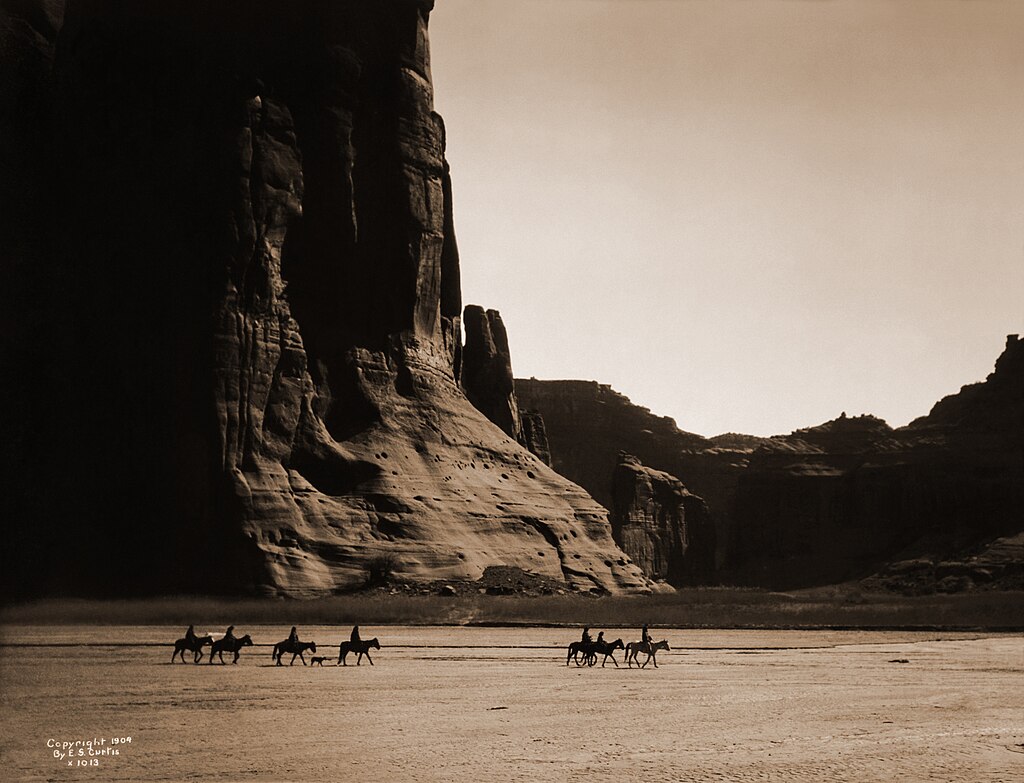 Sept cavaliers et un chien cheminent dans le canyon de Chelly en Arizona, photographie d'Edward Sheriff Curtis prise en 1904.  (définition réelle 3 619 × 2 667)