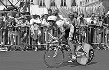 Schwarz-Weiß-Foto eines Mannes mit weißem Helm beim Fahrradfahren