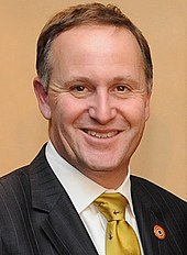 A smiling man wearing a white shirt with a green tie and black jack