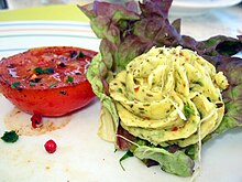 Photo of herb butter in rosette form on lettuce, next to it a halved tomato