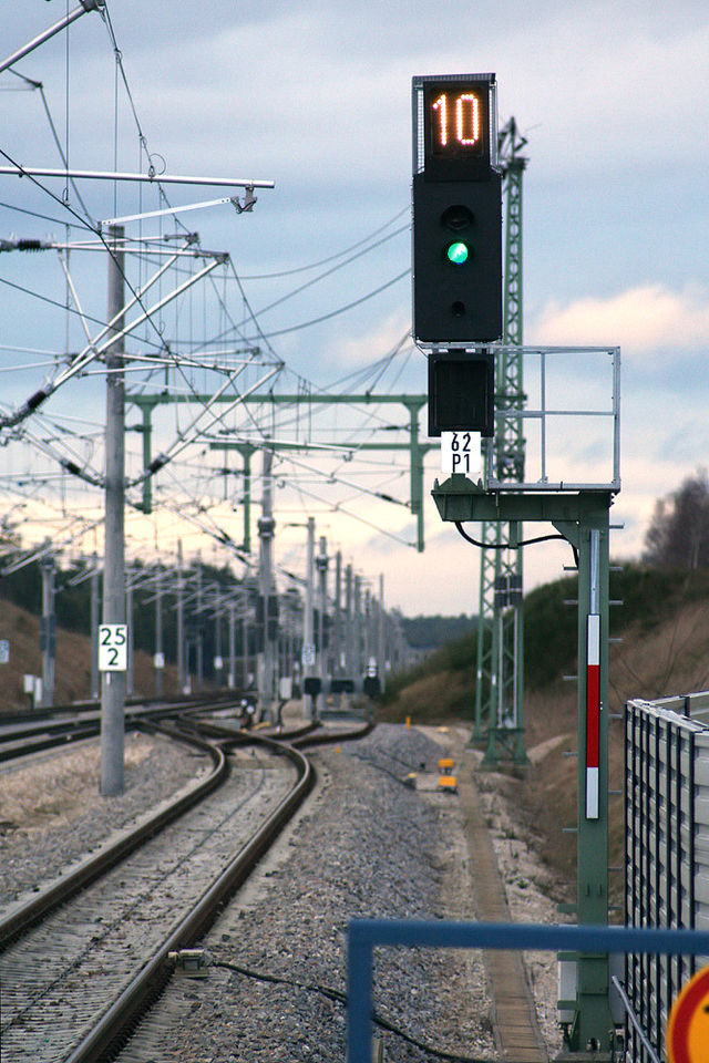 Das Bild zeigt ein Ks-Signal in Allersberg in der Funktion eines Hauptsignals. Zu sehen ist das Signal Ks 1 (ein grünes Licht) und darüber das Signal Zs 3 – Geschwindigkeitsanzeiger (eine weiß leuchtende Kennziffer), das eine 10 zeigt. Dieses Signal erlaubt die Fahrt mit 100 km/h.