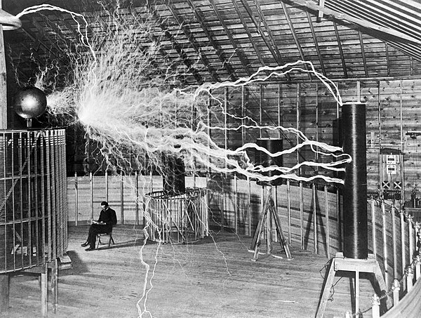 Nikola Tesla sitting in the Colorado Springs Experimental Station with his "magnifying transmitter" generating millions of volts