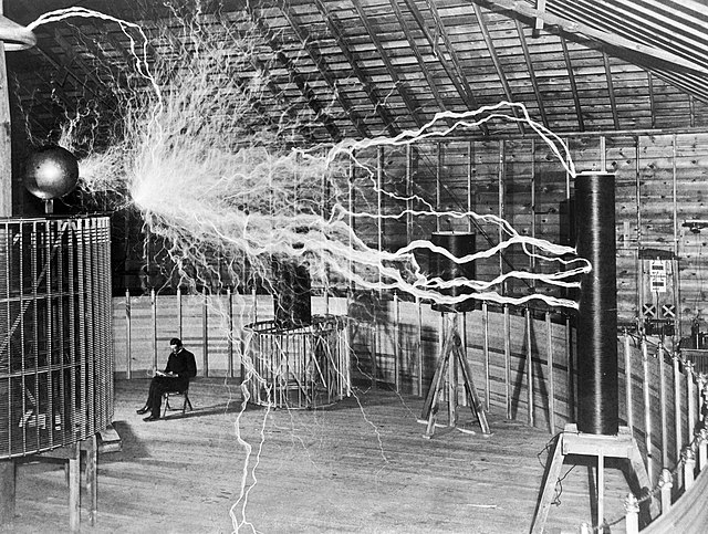 Nikola Tesla sitting in the Colorado Springs Experimental Station with his "magnifying transmitter" generating millions of volts