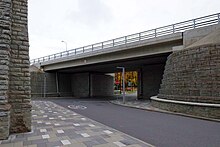 Melengkung batu kapur menara yang mendukung jembatan yang melintas di atas jalan modern.