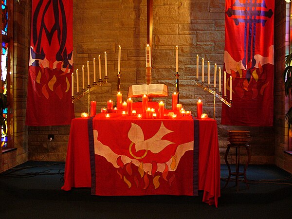 A Protestant church altar, decorated for Pentecost with red burning candles and red banners and altar cloth depicting the movement of the Holy Spirit