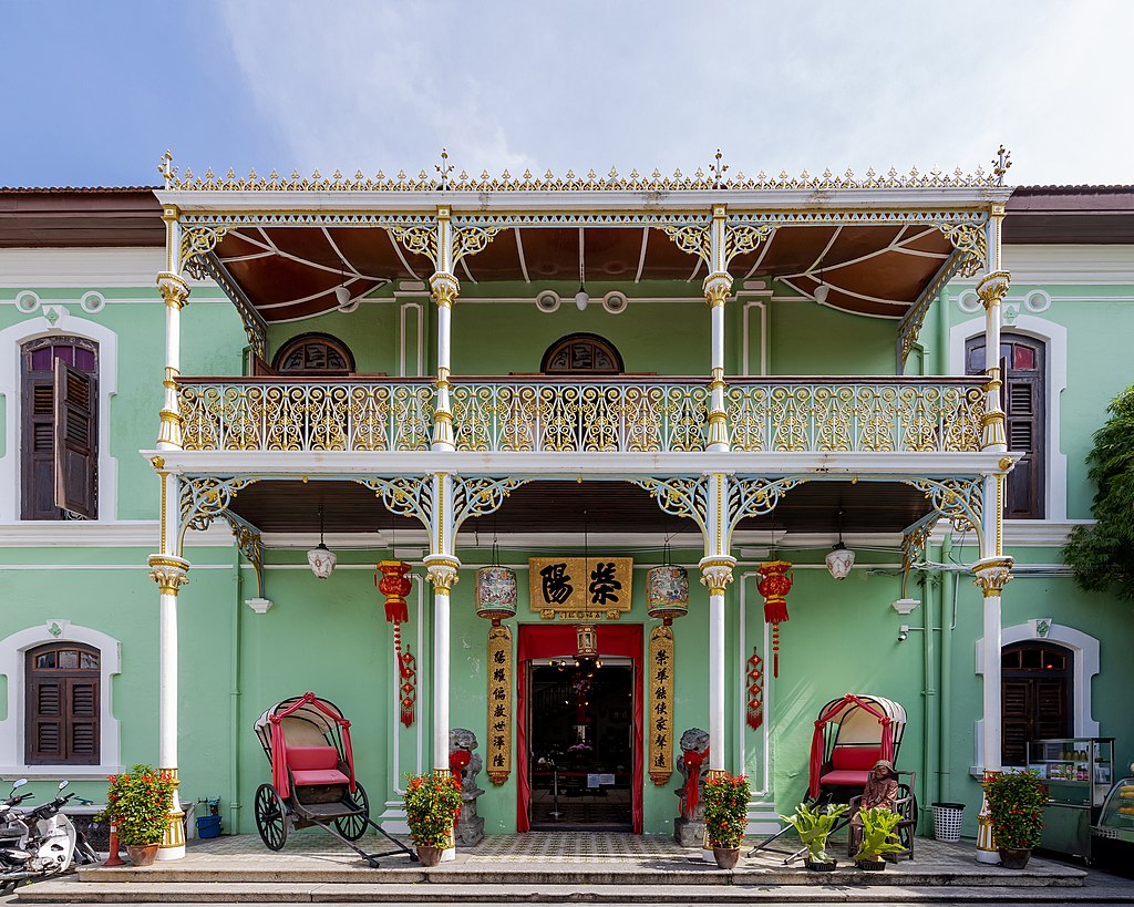 Green 2 storey colonial mansion with ornate balcony and 2 trishaws.
