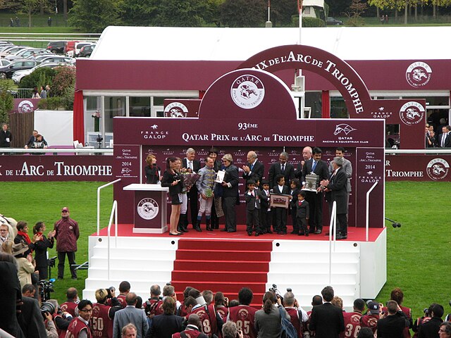 Photo lointaine d'un podium avec plusieurs personnes. Devant celui-ci figurent des photographes.