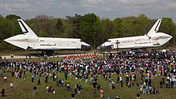 Enterprise a Discovery se setkávají na svém podvozku, zdánlivě nos na nos, po dlážděné cestě na letišti Dulles.  Dav lidí stojících na trávě v popředí se shromáždil, aby viděli podívanou.  Oba orbitery mají aeroskořápky pokrývající prostor motoru.