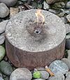 Malý plamen vycházející z válcové betonové desky obklopené kameny