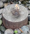 A small flame coming from a cylindrical concrete slab surrounded by rocks