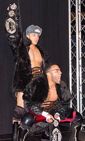 Forever Hooligans, Alex Koslov and Rocky Romero (right), with both the IWGP Junior Heavyweight Tag Team Championship and ROH World Tag Team Championship belts in 2013 Forever Hooligans at ROH.jpg