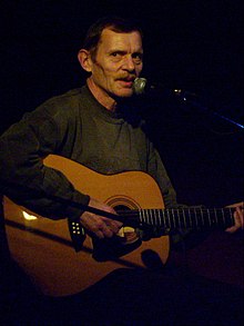 Jiří Schmitzer sentado, tocando la guitarra, mirando a la derecha a la cámara