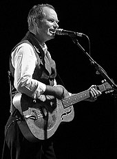 Image en noir et blanc d'un homme jouant de la guitare et chantant dans un micro