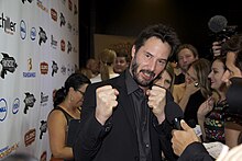 A photo of Keanu Reeves jokingly holding his fists up towards the camera