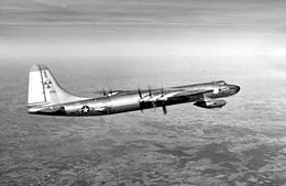 Fotografía en blanco y negro de un avión en vuelo, con la superficie terrestre al fondo.