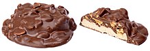 Zwei Ansichten eines Schokoriegels: das ganz linke Ganze zeigt einen schokoladenüberzogenen Hügel mit hervorstehenden Nüssen und die rechte Hälfte zeigt einen mit Erdnüssen belegten Nougatboden und beide mit Schokolade überzogen.