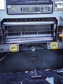 Paper cutting machine with two separate hand buttons and one leg pedal for its operation. Requiring most of the operator's limbs to be used to activate the machine prevents them from being in dangerous positions while it operates. Paper cutting machine with two-handed safety switches.jpg