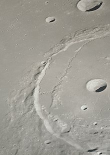 Oblique view of Posidonius from Apollo 15. A tightly convoluted sinuous rille crosses the raised floor of the crater, turns back, and follows the rim to a low point in the western rim. Posidonius crater AS15-91-12366.jpg