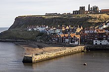 A stone pier with the east cliff of Whitby behind with houses, the church and the abbey