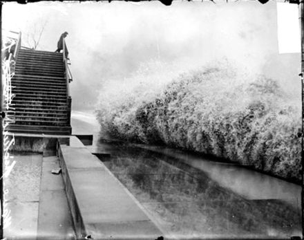 A wave breaking on the shore of Lake Michigan in Chicago while a man watches from a bridge