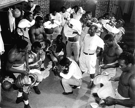 Coach Jake Gaither (standing, middle, white shirt with whistle) in the locker room with his Florida Agricultural and Mechanical University (FAMU) football team: Tallahassee, Florida, 1953