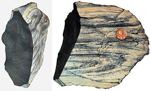 Two lumps of grey rock with some brownish stripes. Weathered surface on right; fresh surface on left.