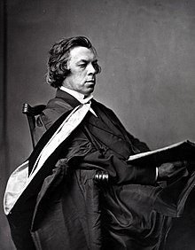 Black and white photograph of John Caird, seated wearing a graduation gown