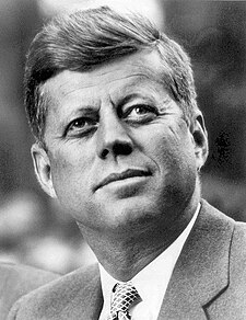 John F. Kennedy (pictured) suggested a lyric from "Washington, My Home" replace the state's motto Alki. John F. Kennedy, White House photo portrait, looking up.jpg