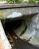 A large, concrete tube with a creek flowing into it.