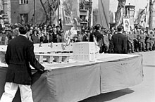 Fotografía en blanco y negro de un modelo blanco de un estadio.  Detrás del modelo, una multitud lo mira.