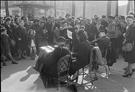 Des musiciens se produisent dans une rue de Paris au printemps 1945. Plusieurs soldats américains figurent parmi la foule.