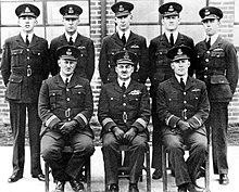 Portrait de groupe d'officiers militaires en uniforme. Cinq hommes sont debout côte à côte à l'arrière, tandis que trois sont assis à l'avant.