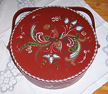 Photographie en plongée d'une soupière rouge dont le couvercle est orné de motifs floraux verts et blancs rayonnant à partir de son centre.