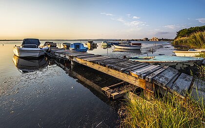 Embarcações na lagoa de Thau (em francês: étang de Thau). Ao fundo, o bairro "Île de Thau" em Sète, Hérault, França. A lagoa de Thau é o maior corpo de água da região da Occitânia. Possui uma área de cerca de 7 500 hectares e uma profundidade média de cinco metros (sendo o ponto mais profundo a nascente do Vise, também chamado buraco do Bisse, que atinge uma profundidade de 32 m). Seu tamanho e sua profundidade, que a distinguem das lagoas da região, são explicados pela geomorfologia do setor; é o sinclinal de uma dobradura cujo anticlinal é a montanha Gardiole a nordeste. A lagoa está ligada ao mar Mediterrâneo por estreitos canais em Marseillan e Sète. (definição 6 475 × 4 051)