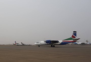 A colourful twin-engine aircraft taxiing on a dusty airport apron under a grey sky