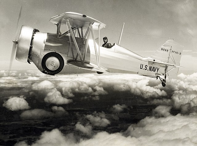 Curtiss XF11C-3 variant flying over the clouds with landing gear and tailhook retracted