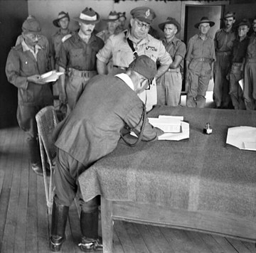 Masao Baba, Lieutenant General of the Japanese 37th Army signs the surrender document in Labuan, British Borneo, being watched by Australian Major General George Wootten and other Australian units.